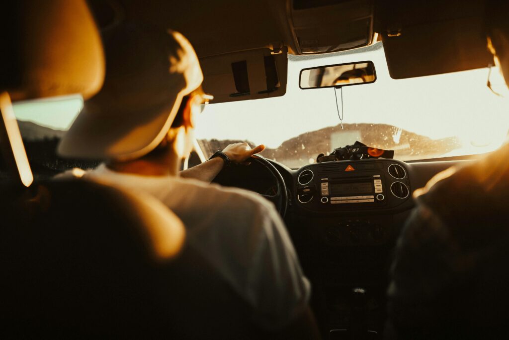 Man driving car with passenger at sunset, capturing warm sunlit atmosphere.